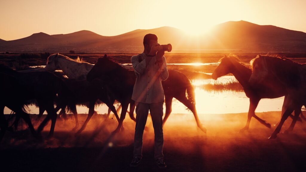 A photographer at sunset surrounded by galloping horses