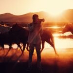 A photographer at sunset surrounded by galloping horses