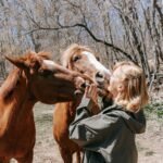 A woman interacting with two horses in a wooded setting