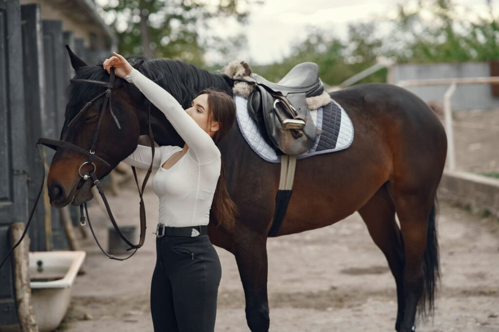 A woman adjusting a horse bridle outdoors, preparing for a grooming or tacking session