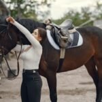 A woman adjusting a horse bridle outdoors, preparing for a grooming or tacking session