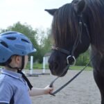 A child in a riding helmet leading a horse at a ranch