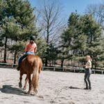 A rider and instructor during a horseback riding lesson in an outdoor arena
