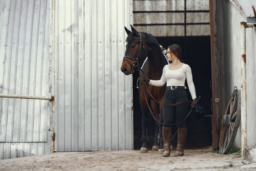 A young woman leading a horse by the reins out of a barn
