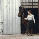 A young woman leading a horse by the reins out of a barn