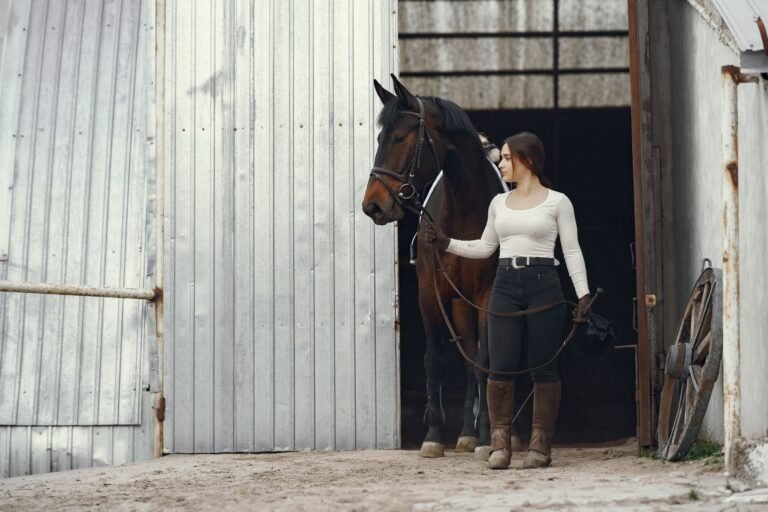 A young woman leading a horse by the reins out of a barn