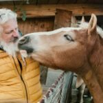 A bearded man in a yellow jacket handling a horse outdoors