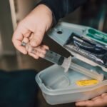 A hand holding a syringe from a medical kit with supplies